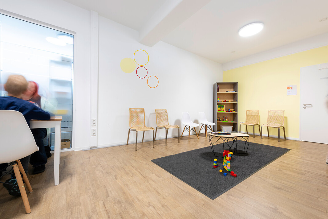 Wartezimmer mit Stühlen und Spielecke für Kinder auf einem dunklen Teppich.
